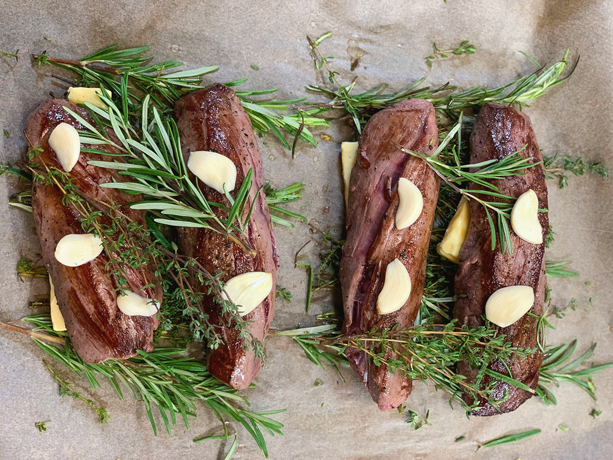 game meat with garlic and rosemary on baking tray