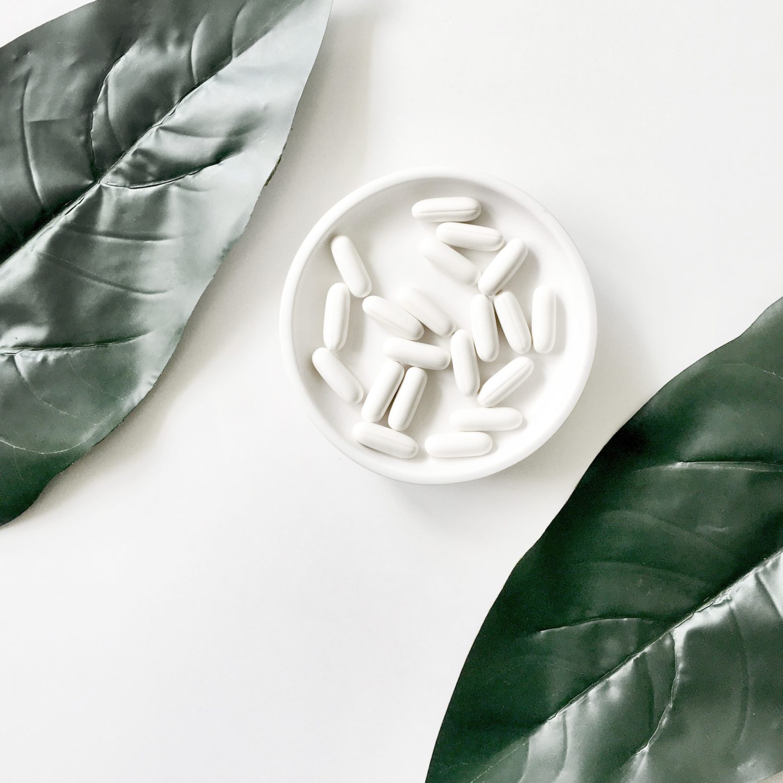 Supplements in a bowl, green leaves surrounding it