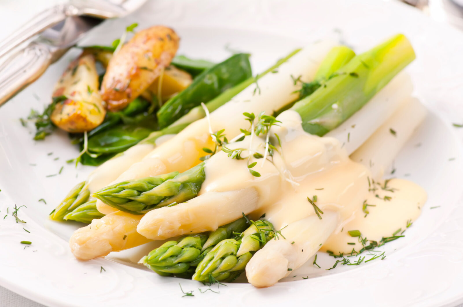 Asperges blanches et vertes avec sauce hollandaise sur une assiette blanche.