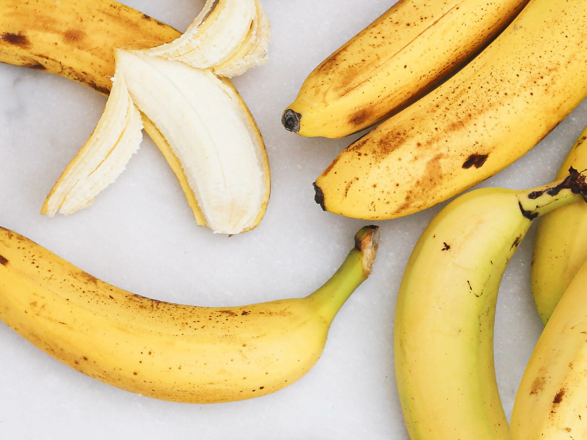 Several bananas on white background, one partly unpeeled