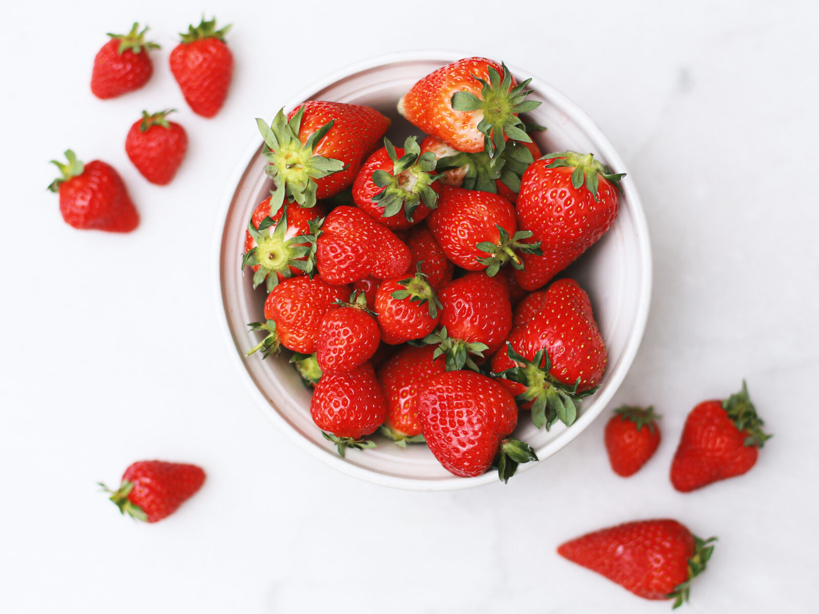 Strawberries in and around a white bowl