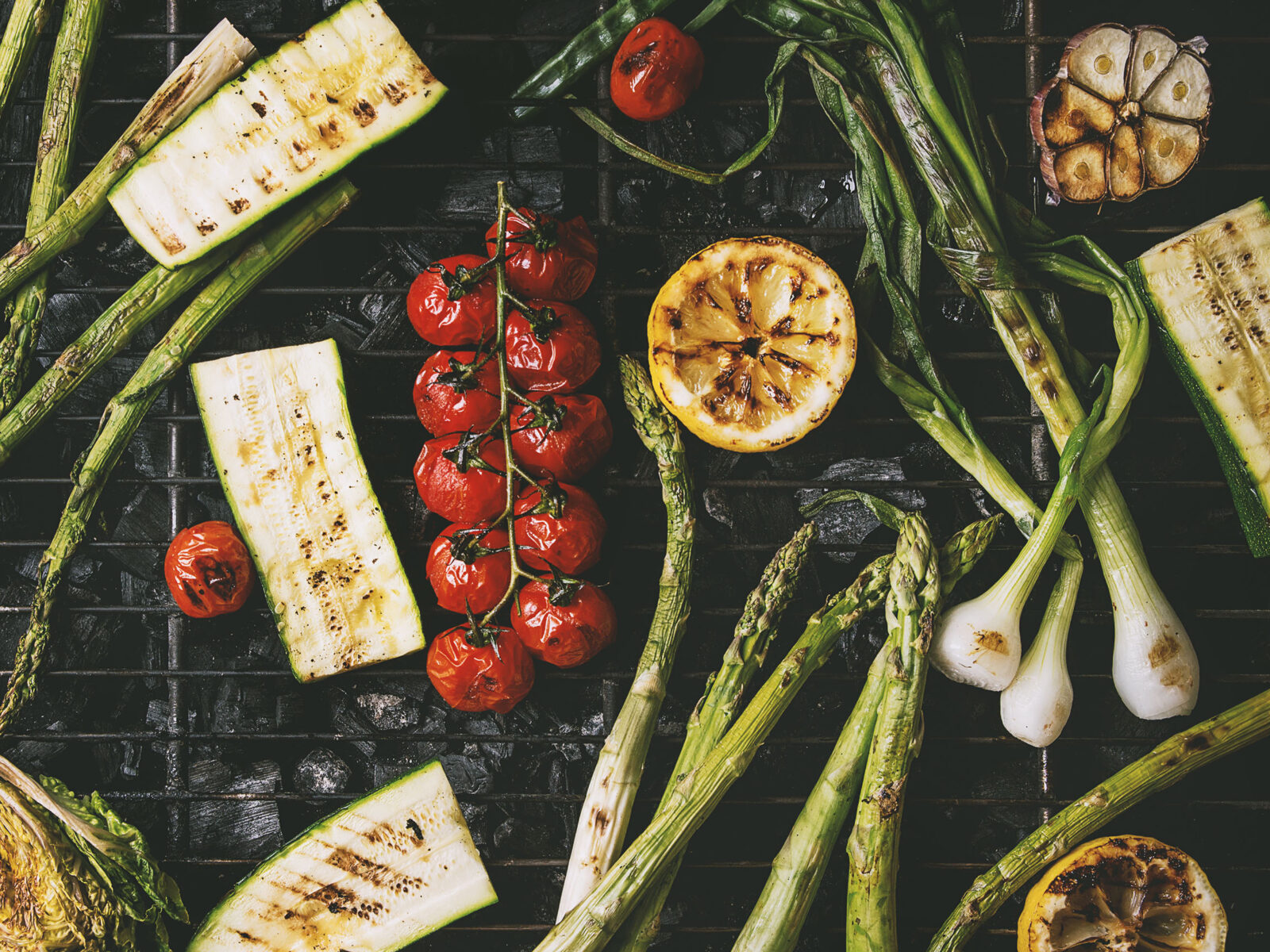 Spring onions, cherry tomatoes, courgette and lemon slices on a charcoal grill roast