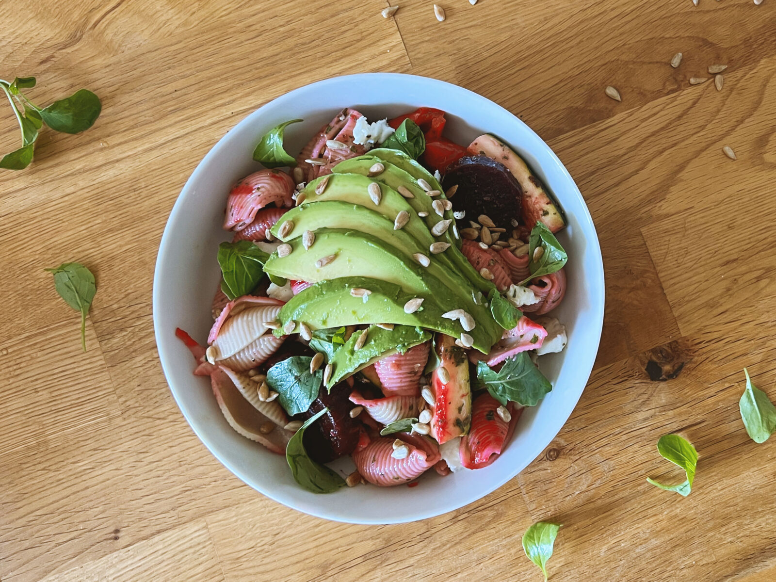 Pastasalat mit Avocado, Zucchetti und Randen auf einem Holztisch