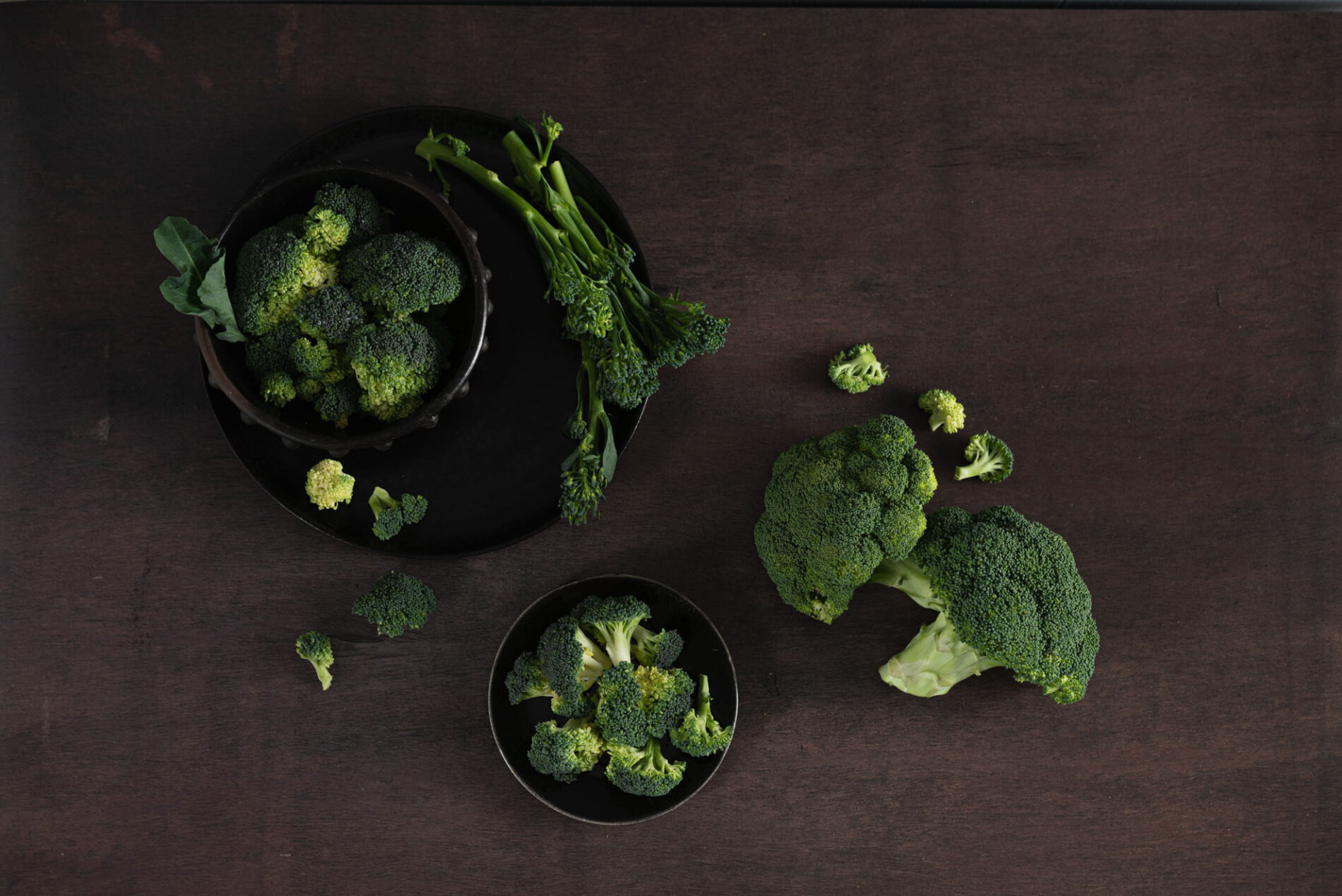 broccoli florets and heads arranged on dark brown surface