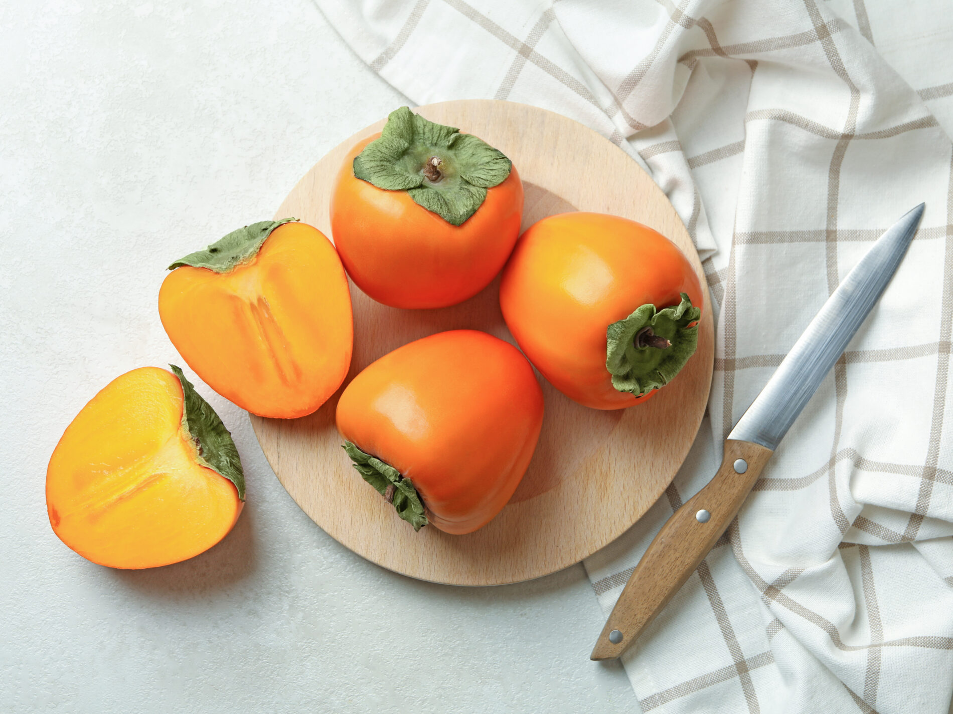 Plate with persimmon, knife and kitchen towel on white table