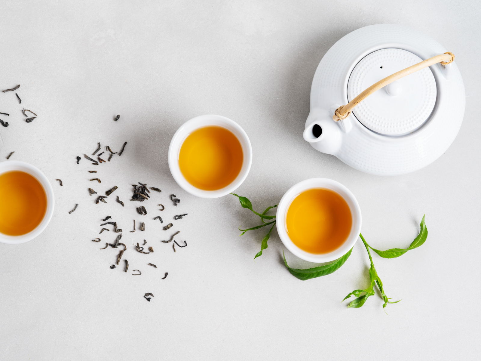 Tea pot and three filled tea mugs next to scattered tea leaves