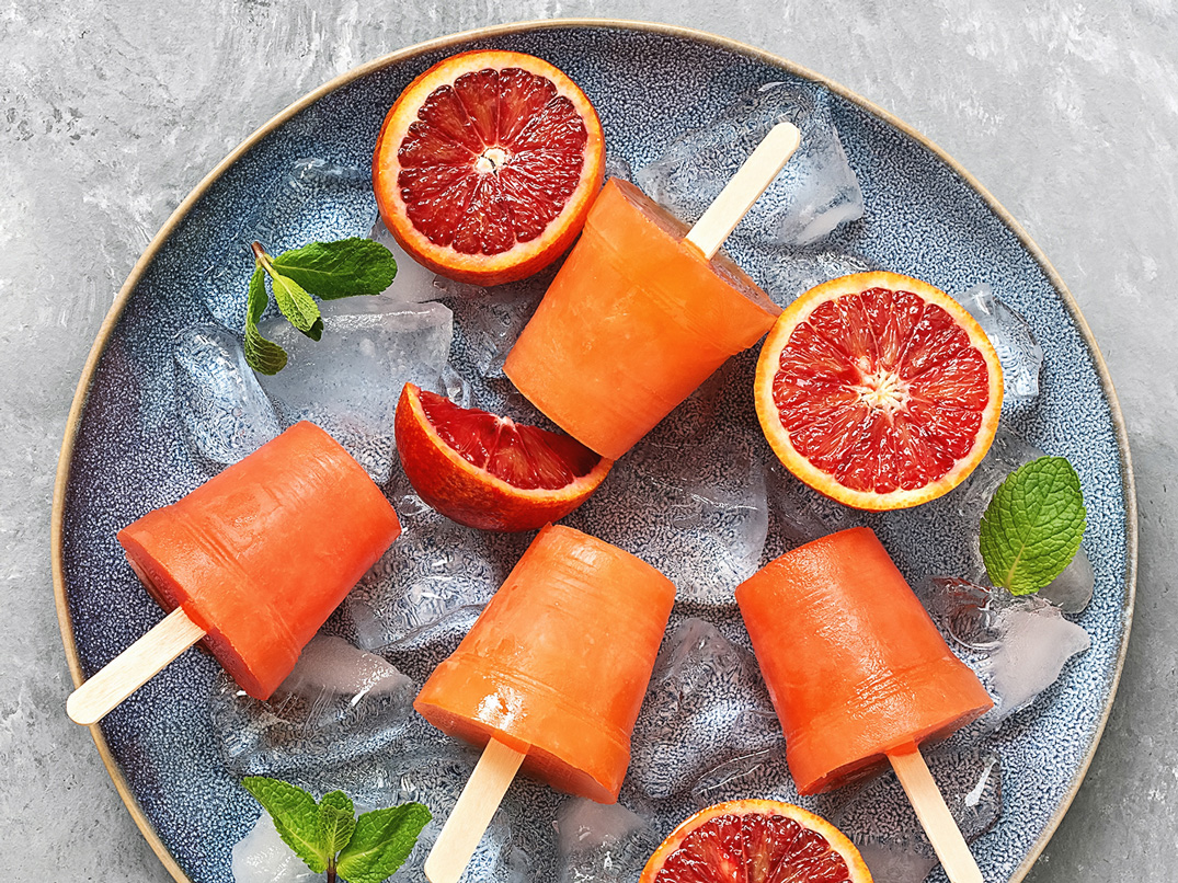 Blood orange sorbet on sticks, lying on ice cubes and surrounded by blood orange slices