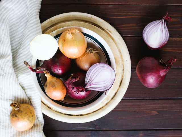 white bowl on a wooden table with red onions and white onions